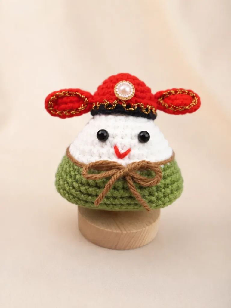 10 Minute Crochet Projects for Beginners 4 Cute crochet acorn doll amigurumi with a red hat, green body, black eyes, and brown bow displayed on a neutral beige background.