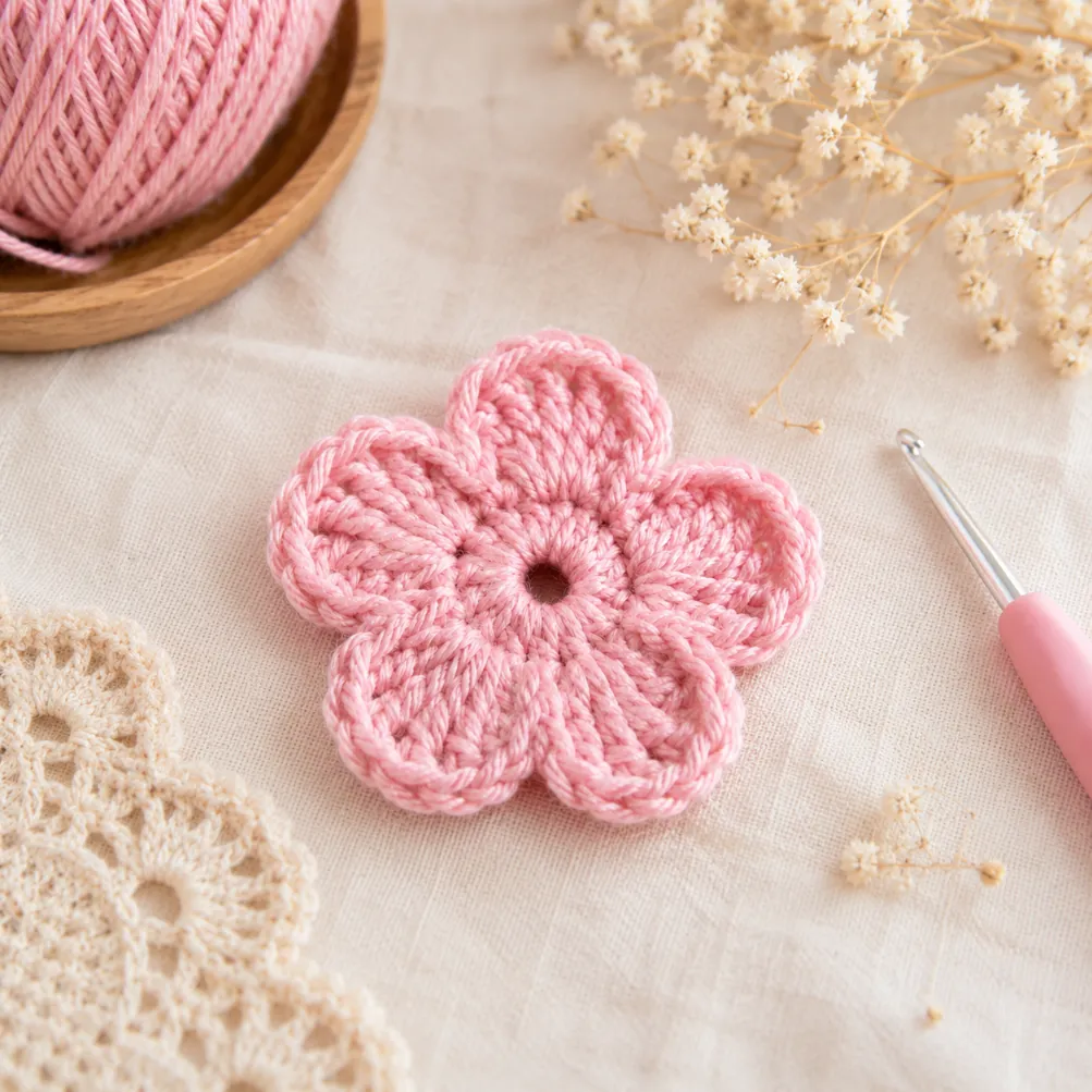 Best Small Crochet Projects for Beginners 4 Pink crochet flower applique with soft handmade petals displayed in a cozy crochet workspace with yarn and crochet tools.