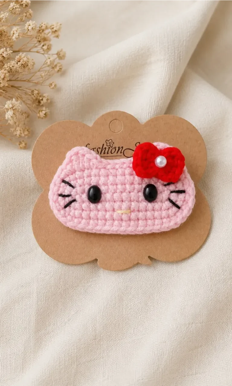 Kitty Hair Clip Crochet Pattern for Beginners (So Easy And Free!) 8 Finished Kitty Hair Clip Crochet Pattern featuring a pink crochet cat face with black safety eyes, embroidered whiskers, a red bow, and a pearl accent attached to a snap hair clip.